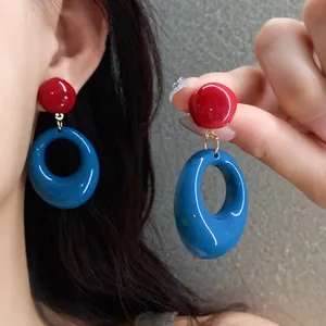 Macro detail view of retro red and blue resin oval drop earrings being worn and held