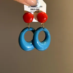 Close-up of retro oval resin drop earrings featuring vibrant red and blue color blocking design