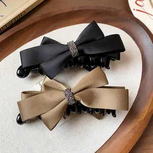 Détail de barrettes à nœud en satin élégantes en noir et beige avec centre en strass.
