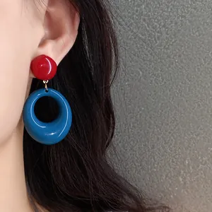 Close-up detail view of vintage red and blue resin hoop pendant earrings worn on ear