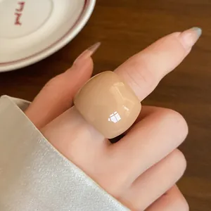 Dettaglio di un anello minimalista in resina beige lucido indossato sull'indice