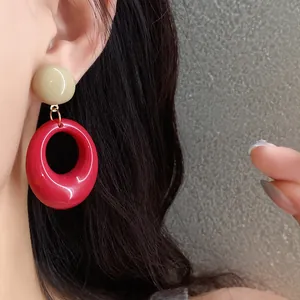 Close-up detail of vintage red and khaki resin oval pendant earrings on model.