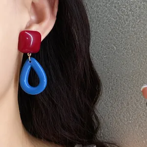 Detailed side view close-up of vintage style red and blue resin pendant earrings worn on ear