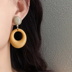 Close-up detail of vintage resin oval drop earrings in mustard yellow and sage green on model