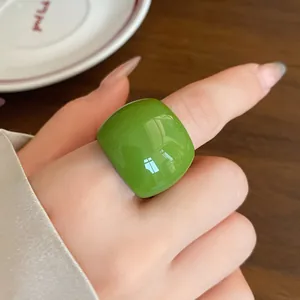 Dettaglio di un anello in resina verde lucido dalla forma quadrata arrotondata e audace.
