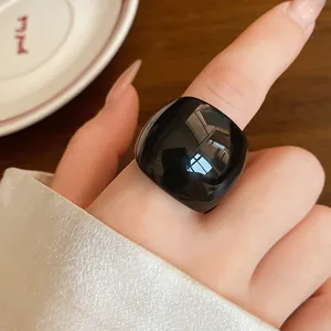 Primo piano di un anello quadrato in resina nera lucida indossato all'indice in stile minimal