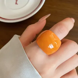 Dettaglio ravvicinato di un anello quadrato in resina arancione indossato su un dito