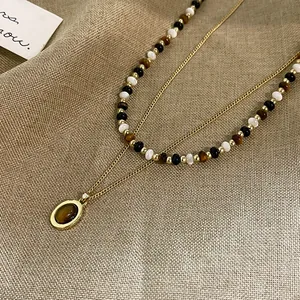 Dettaglio di una collana a strati con perle occhio di tigre e catena d'oro in lino