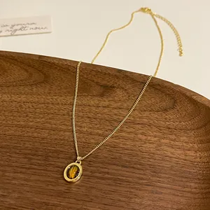 Vista dettagliata della collana con ciondolo occhio di tigre e catena d'oro su legno.