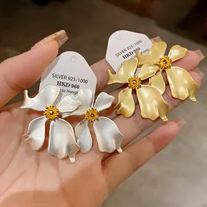 Primer plano de pendientes de flores mate en plata y oro con estambres amarillos
