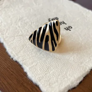Detalle macro de un anillo abierto triangular dorado vintage con rayas de cebra negras