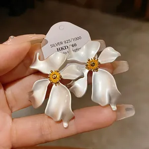 Primer plano de pendientes de flores blancas grandes con centro amarillo y plata.