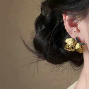 Dettaglio di un orecchino a farfalla vintage dorato con strass blu all'orecchio
