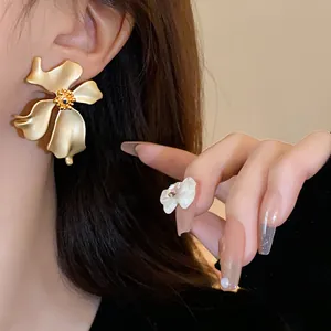Primer plano de un pendiente de flor en oro mate, estética vintage elegante y femenina.