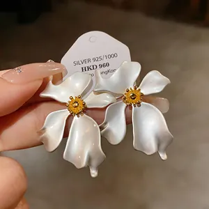 Primer plano de elegantes pendientes de flores blancas con aguja de plata 925 y brillo perlado.