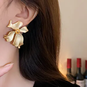 Primer plano detallado de un elegante pendiente de botón de oro mate con forma de flor en la oreja