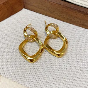 Primer plano de pendientes de rombo retorcidos dorados con pavé de circonitas brillantes.