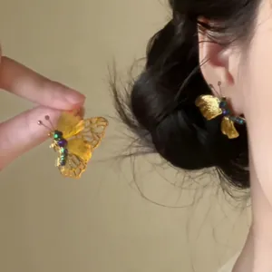 Dettaglio di orecchini a farfalla dorati vintage con perline delicate indossati sull'orecchio.