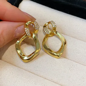 Detalle de pendientes geométricos dorados con circonitas sobre textura de tela beige