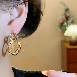 Detalle de pendientes de botón entrelazados dorados con piedras de circonita pavé