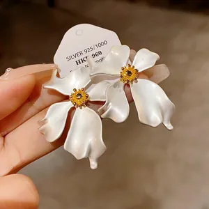 Primer plano de elegantes pendientes de flores blancas estilo vintage con acabado perlado y oro.