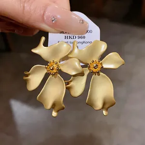 Vista detallada de pendientes vintage con forma de flor en oro mate y agujas de plata.