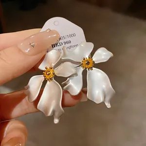 Primer plano de elegantes pendientes de flores blanco nácar con tachuelas doradas.
