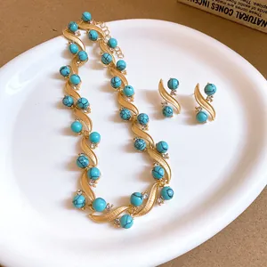 Close-up of vintage gold necklace and earrings set with turquoise beads on a white plate.