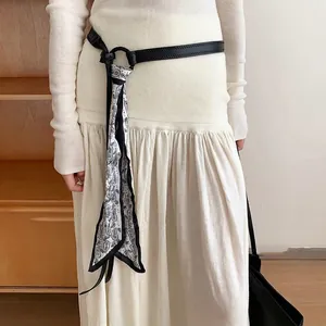 Dettaglio di cintura in pelle nera con elegante sciarpa in seta stampata paisley