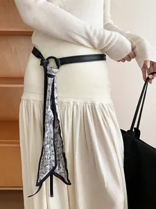 Dettaglio di una cintura in pelle con foulard in seta a motivo paisley su abito bianco.