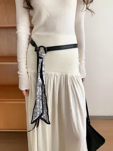 Dettaglio di una cintura in pelle nera con foulard in seta paisley su un vestito bianco