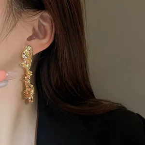 Primo piano dettagliato di eleganti orecchini a nappa in metallo liquido dorato su modella