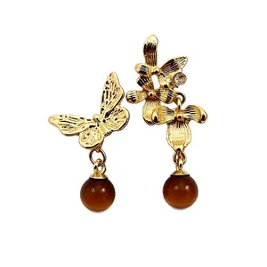 Orecchini asimmetrici vintage a farfalla e fiore con perle marroni su sfondo bianco pulito