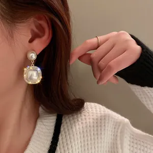 Dettaglio di eleganti orecchini pendenti in perle quadrate con bordo in strass sul modello.