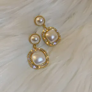 Dettaglio macro di orecchini vintage francesi con perle e cristalli su pelliccia bianca.