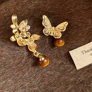 Dettaglio macro di orecchini asimmetrici a fiore e farfalla dorati con perline marroni