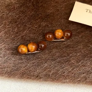 Orecchini con tre perle stile Maillard su sfondo di finta pelliccia marrone dettaglio