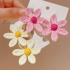 Detailed view of woven flower stud earrings in pink and white on a display card