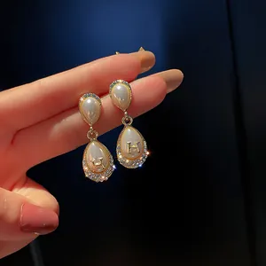 Dettaglio di orecchini vintage in perla e oro con lettera H e cristalli scintillanti