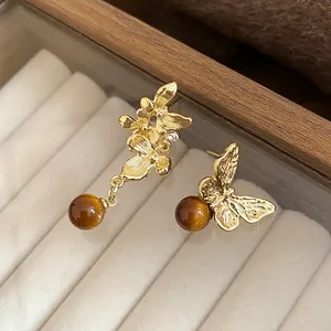 Vista ravvicinata di orecchini asimmetrici a fiore e farfalla con perle marroni.
