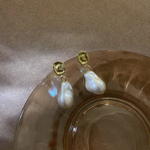 Dettaglio di orecchini a goccia con perle barocche vintage su piatto di vetro ambra.