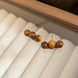 Primo piano di orecchini a lobo asimmetrici con perle marroni Maillard e dettaglio oro