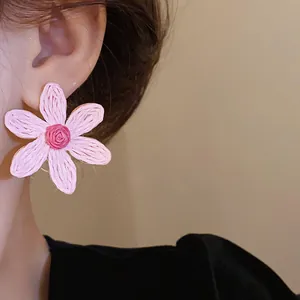 Close-up of pink woven flower stud earring on ear with bohemian handmade texture