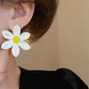 Detailed close-up view of a bohemian white woven daisy flower stud earring on ear