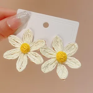 Detailed view of handmade woven daisy flower earrings with white and yellow accents