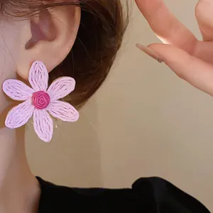 Detailed close-up view of pink woven flower stud earrings worn by an Asian model