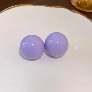 Orecchini a perno a sfera viola minimalisti presentati su un piatto decorativo bianco.