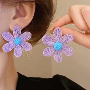 Macro detail of purple woven flower stud earrings with blue center and steel needle