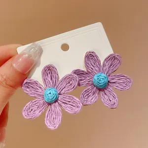 Macro view of purple and blue woven bohemian flower stud earrings on white card