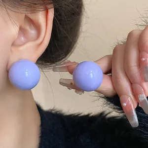 Dettaglio macro di eleganti orecchini a sfera viola lucidi con solidi perni in argento